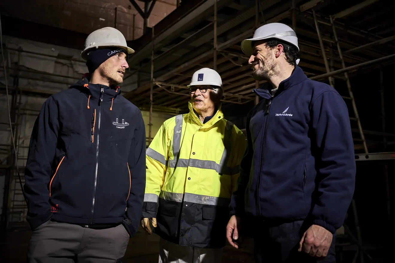 Trois hommes en casque de chantier discutent sur le chantier du Canopée
