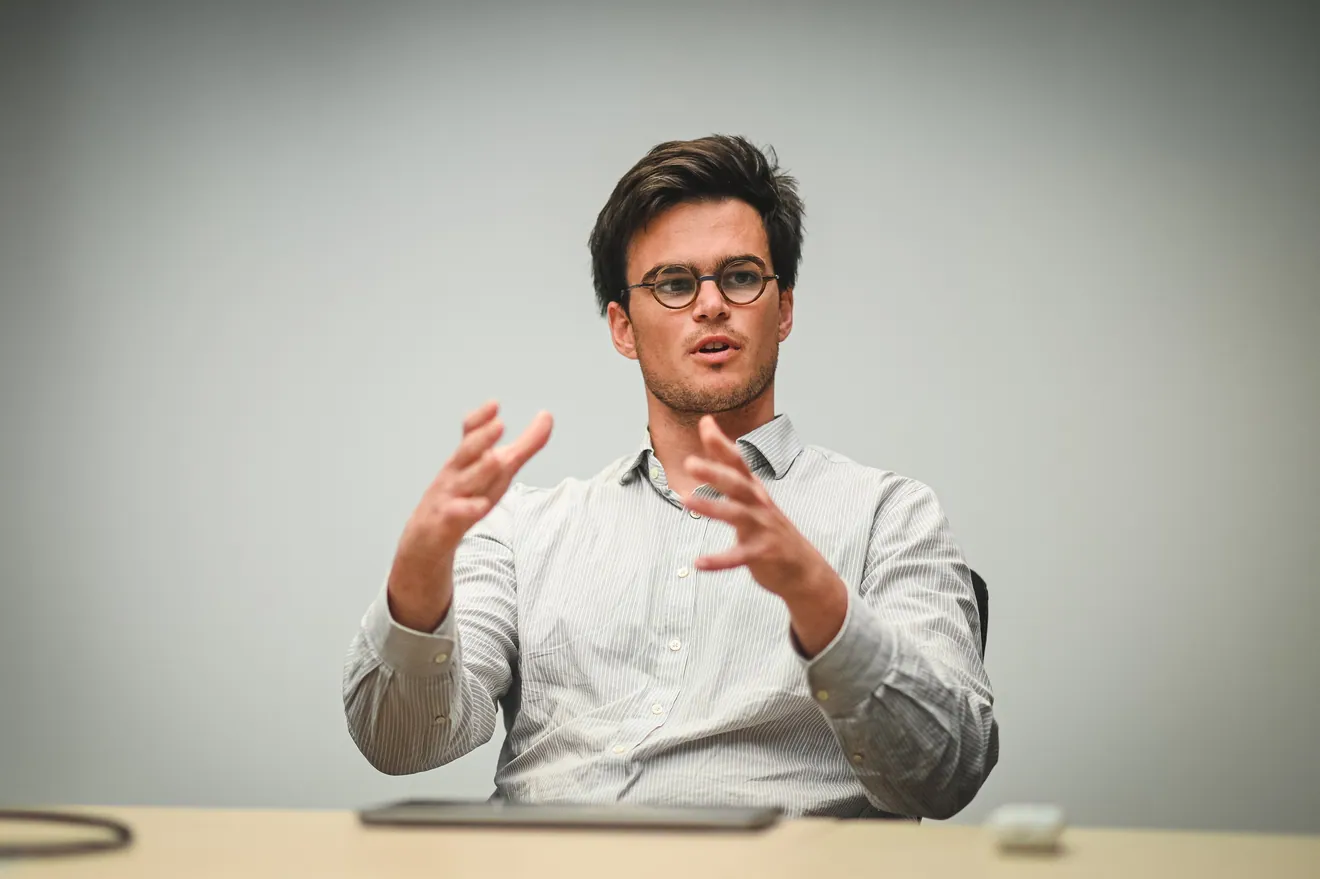 Un homme à lunettes s’exprime, assis à une table