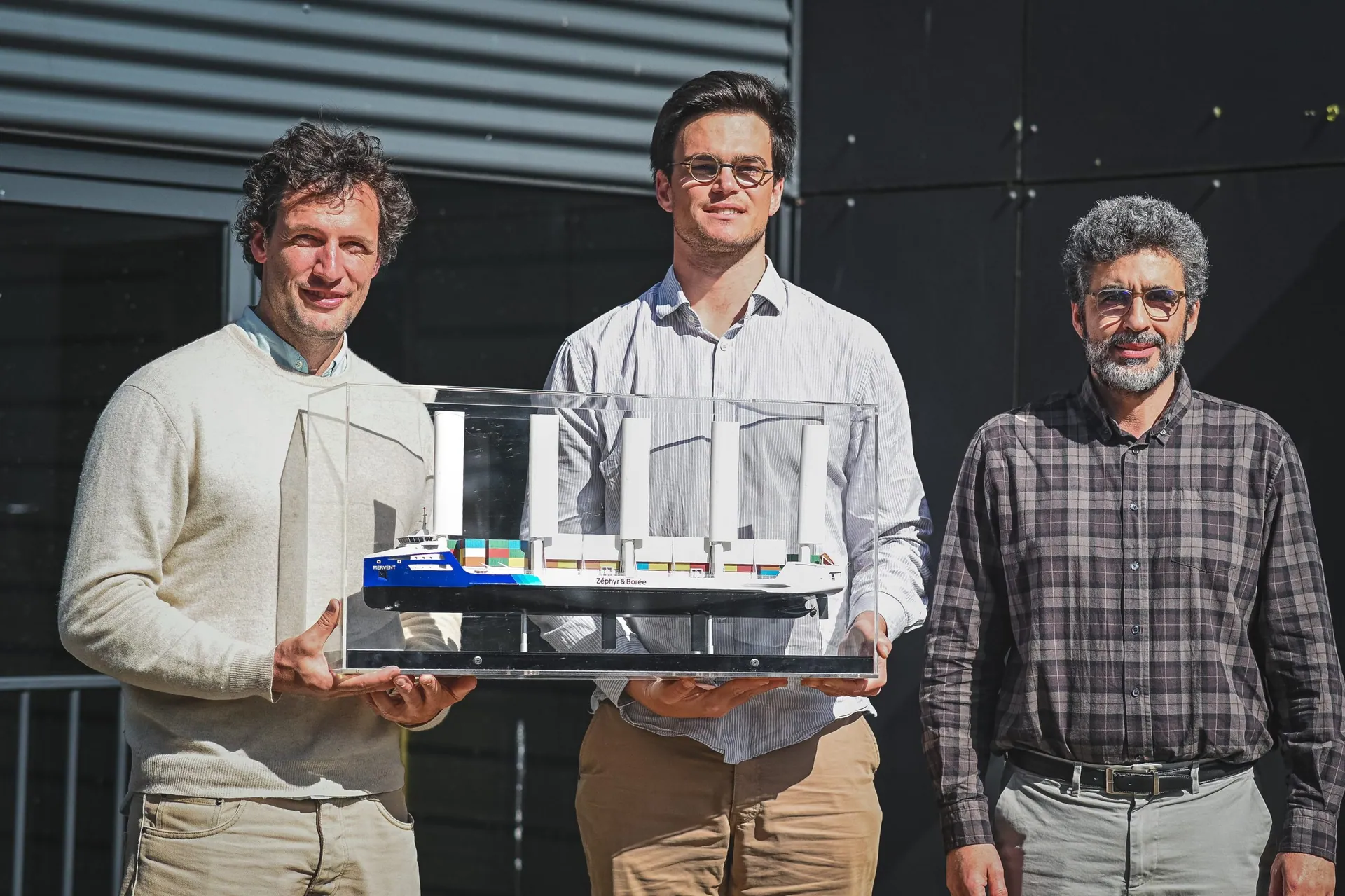 Trois hommes présentent la maquette du porte-conteneurs à voiles Williwaw