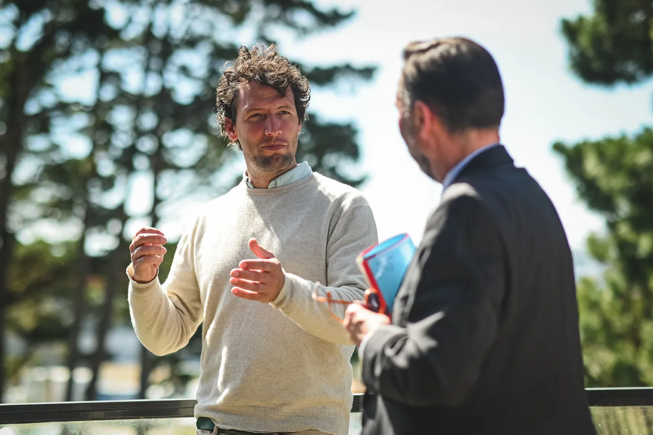 Deux hommes en discussion sur une terrasse, devant des pins