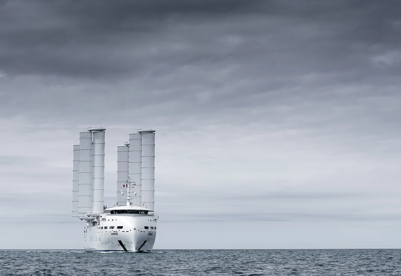 Le cargo à voiles Canopée en mer, ses quatre ailes déployées, sous un ciel gris