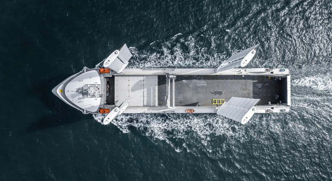 Vue zénithale du cargo à voiles Canopée en mer, ses quatre ailes déployées de part et d’autre du pont