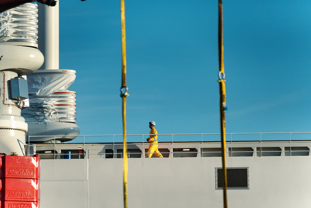Membre d'équipage marchant sur le pont du Canopée entre les élingues jaunes des grues